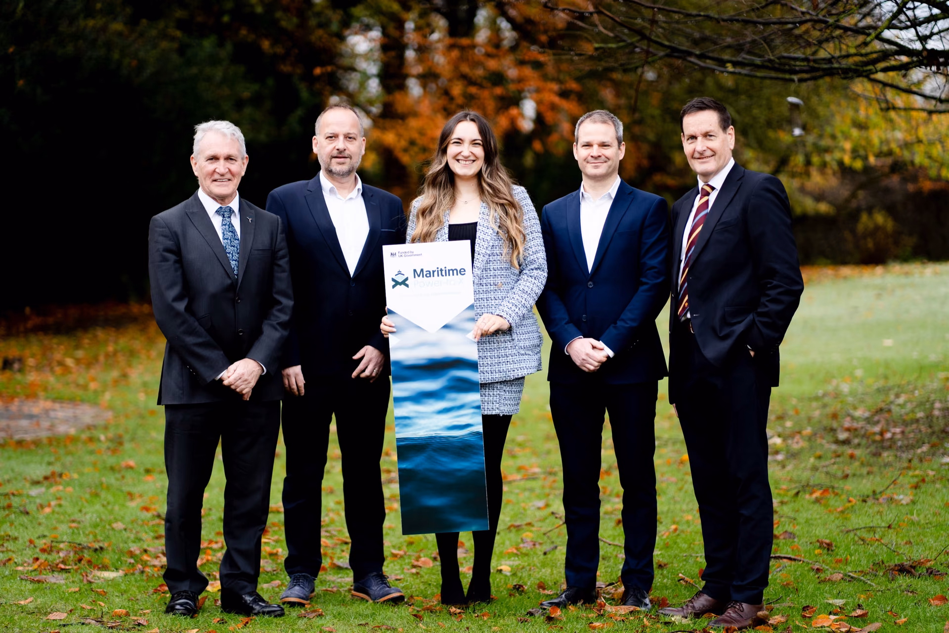 Five people from the B9 team holding a Maritime Power-to-X banner on a lawn